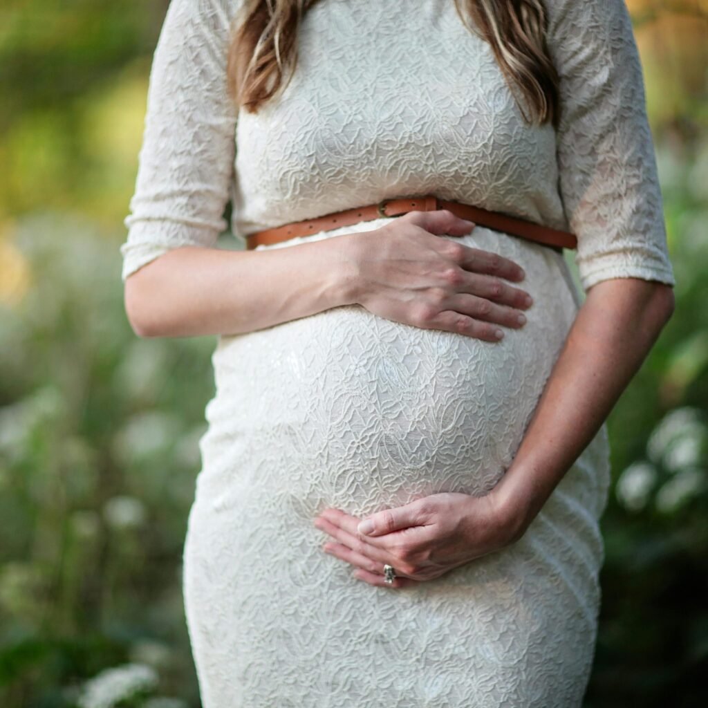 A pregnant woman in a lace dress gently cradling her belly in an outdoor setting.