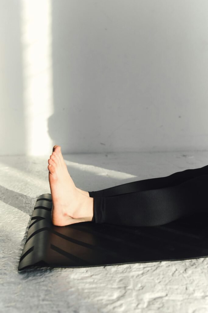 Barefoot yoga position on black mat against a white wall with sunlight.